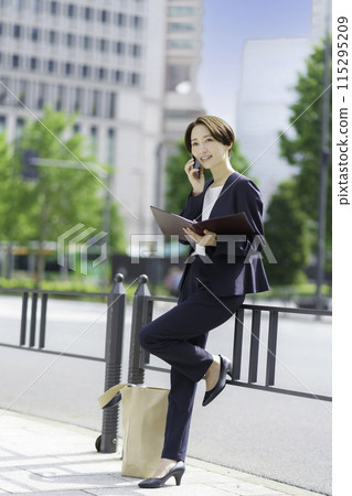 Businesswoman holding a notebook and talking on a smartphone, vertical position 115295209