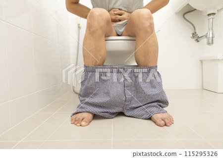 Close up view of man sitting on toilet bowl in rest room Close up view of man sitting on toilet bowl in rest room 115295326