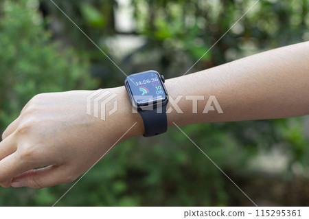 Close up of young woman looking on her smartwatch in the green garden background  115295361