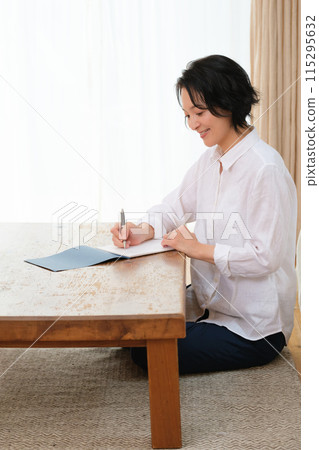A middle-aged woman writing a letter to her family in the living room 115295632