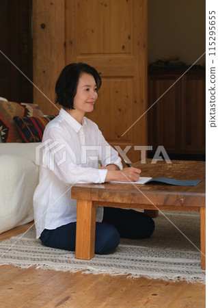 A middle-aged woman writing a letter to her family in the living room A middle-aged woman writing a letter to her family in the living room 115295655