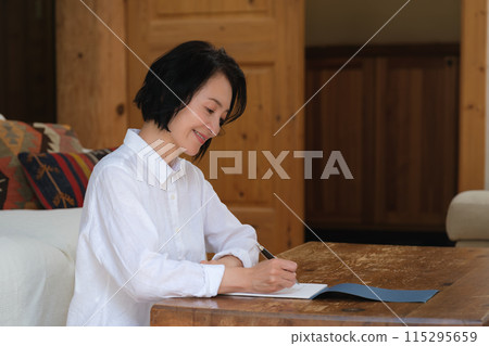 A middle-aged woman writing a letter to her family in the living room 115295659