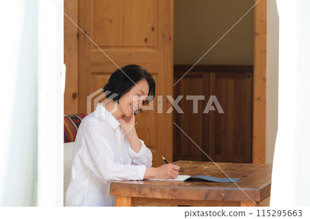 A middle-aged woman writing a letter to her family in the living room 115295663