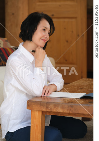A middle-aged woman writing a letter to her family in the living room 115295665