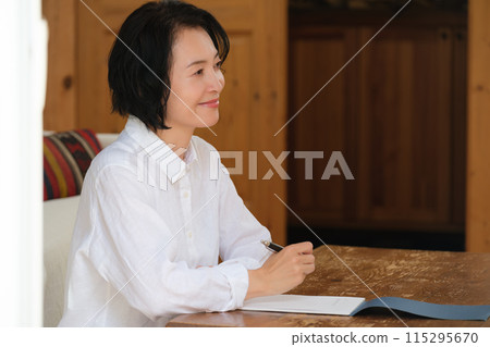 A middle-aged woman writing a letter to her family in the living room 115295670