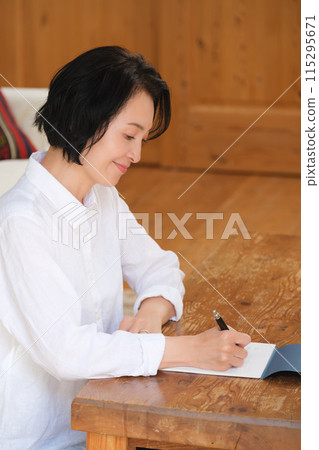 A middle-aged woman writing a letter to her family in the living room 115295671