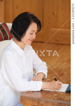 A middle-aged woman writing a letter to her family in the living room A middle-aged woman writing a letter to her family in the living room 115295673