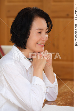 A middle-aged woman writing a letter to her family in the living room 115295696