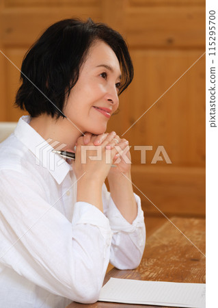 A middle-aged woman writing a letter to her family in the living room 115295700