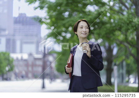 一位女商人站在辦公區，手裡拿著筆記本和飲料的肖像 115295735