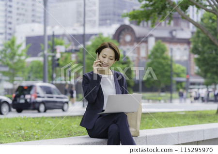 A businesswoman in an office district talking on her smartphone while looking at a laptop 115295970