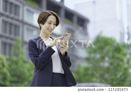 A businesswoman in an office district operating a smartphone 115295973