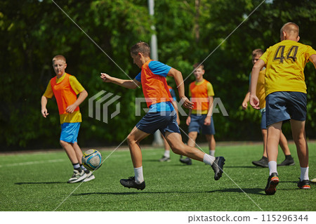 Teamwork in Action. Young soccer players in colorful uniforms playing soccer game outdoors on sunny day. Cooperation and competitive spirit. 115296344