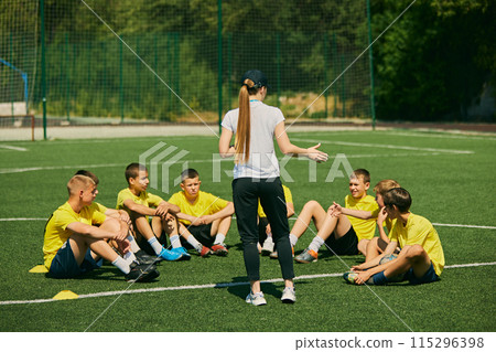 Youth Sports Education. Group of enthusiastic young soccer players listening to strategic advice from female coach, focusing on teamwork and skill development. Youth Sports Education. Group of enthusiastic young soccer players listening to strategic advice from female coach, focusing on teamwork and skill development. 115296398