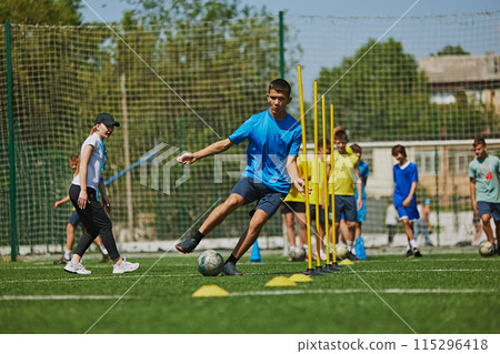 Teamwork and Agility. Young soccer players in uniforms raining outdoors on football field with coach, growing skills and endurance. 115296418