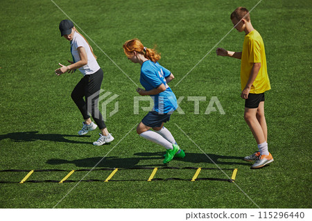 Athletic Training on Field Kids wearing sports gear engaged in challenging footwork exercise with agility ladder equipment. Athletic Training on Field Kids wearing sports gear engaged in challenging footwork exercise with agility ladder equipment. 115296440