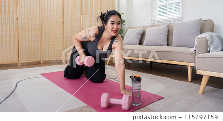 Overweight Woman Engaging in Home Workout Routine with Dumbbells, Showcasing Determination and Healthy Lifestyle Change in Modern Living Room Setting 115297159