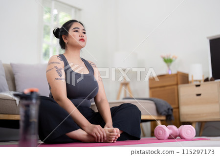 Confident Woman Practicing Yoga at Home, Embracing Healthy Lifestyle and Weight Loss Journey, Sitting on Yoga Mat with Dumbbells in Modern Bedroom, Promoting Fitness and Self Care 115297173