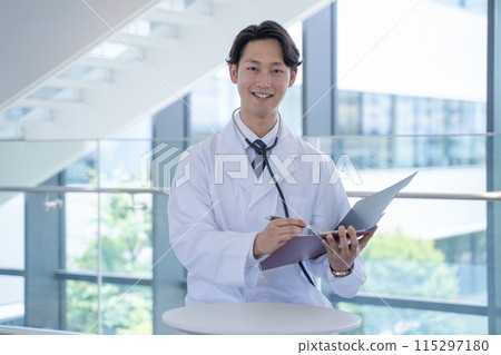 A male doctor smiling and filling out a medical record at the hospital 115297180