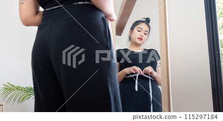 Young woman measuring waist in front of mirror. Concept of fitness and body positivity 115297184