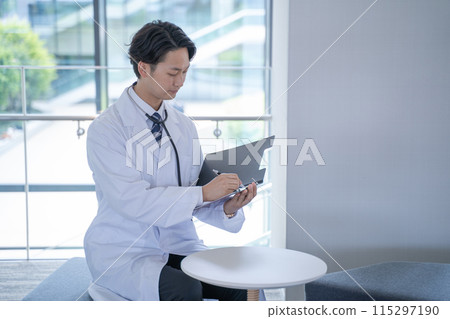 A male doctor smiling and filling out a medical record at the hospital 115297190