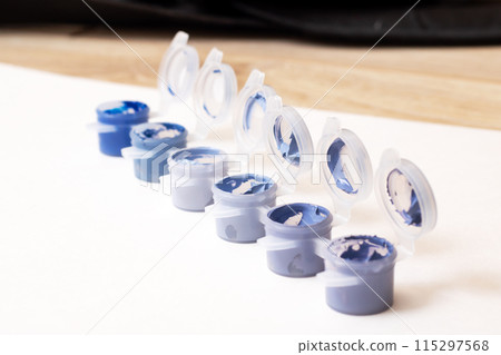 Several containers filled with blue paint are organized in a straight line 115297568