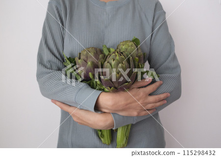 Hands gently holding fresh artichokes, showcasing nature's green bounty with care 115298432