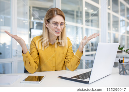 Frustrated businesswoman in a yellow shirt using a laptop in a modern office, feeling confused and unsure while working. Frustrated businesswoman in a yellow shirt using a laptop in a modern office, feeling confused and unsure while working. 115299047