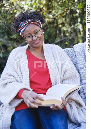 young black woman reading a book sitting on a garden bench. young black woman reading a book sitting on a garden bench. 115300672