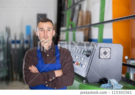 Confident worker standing near machinery control panel in glass processing workshop 115301561