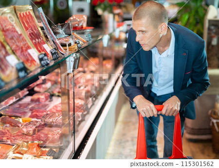 Focused man examines the production in the department of the butcher shop in the supermarket 115301562