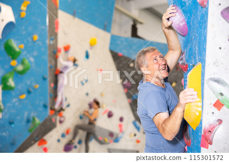 Focused active aged man climbing on bouldering wall 115301572