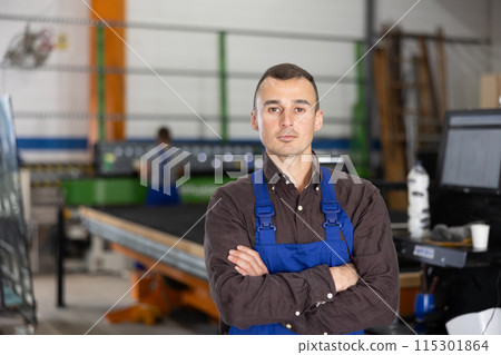 Portrait of positive man in blue overalls in window glass production workshop 115301864