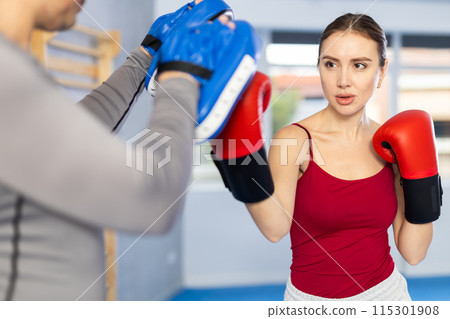 Young girl training boxing kicks on punch mitts held by male instructor Young girl training boxing kicks on punch mitts held by male instructor 115301908