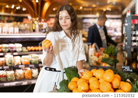 Focused young girl selects ripe tangerines in a supermarket 115302032