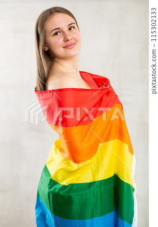 Young teenage girl draped over shoulders, wrapped herself in fabric of Pride flag Young teenage girl draped over shoulders, wrapped herself in fabric of Pride flag 115302133
