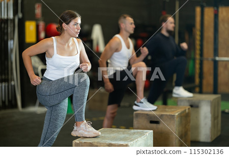 Motivated girl performing step-ups on plyo box during group workout Motivated girl performing step-ups on plyo box during group workout 115302136