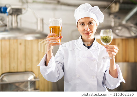 Female brewer examining quality of beer and hop pellets in glasses 115302150