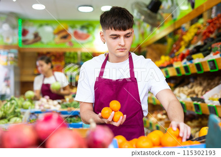 Man store employee displaying assortment of oranges at fruit department in supermarket Man store employee displaying assortment of oranges at fruit department in supermarket 115302193