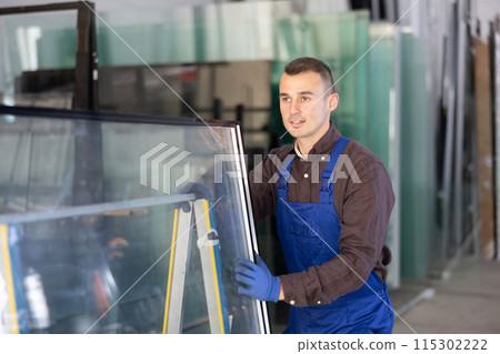 Portrait of man in blue overalls with window panes in glass workshop 115302222