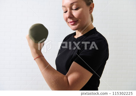 Young sporty female athlete exercising with dumbbell at home gym 115302225