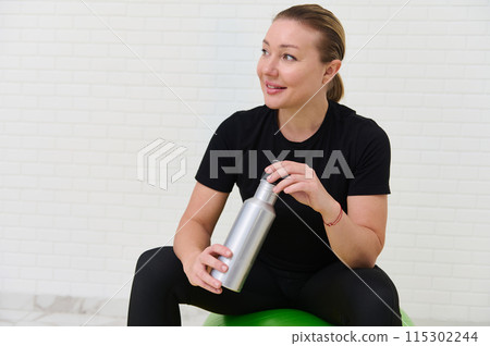 Young sporty woman resting with water bottle after home workout session Young sporty woman resting with water bottle after home workout session 115302244