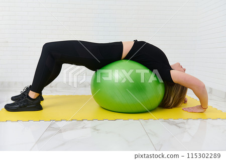 Young athletic woman working out with gym equipment in home studio using a fitness ball 115302289