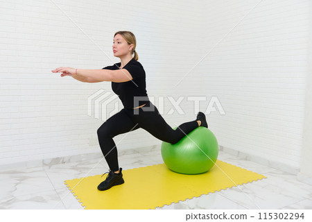 Young sporty female athlete exercising with dumbbells and fitness ball in home studio Young sporty female athlete exercising with dumbbells and fitness ball in home studio 115302294