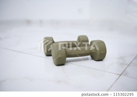 Pair of green dumbbells on white floor in home gym studio for fitness workout 115302295