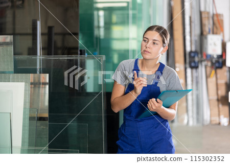 Female worker inspecting glass panels and writing on clipboard in workshop Female worker inspecting glass panels and writing on clipboard in workshop 115302352