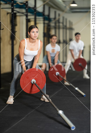 Young woman lifting barbell in gym Young woman lifting barbell in gym 115302353