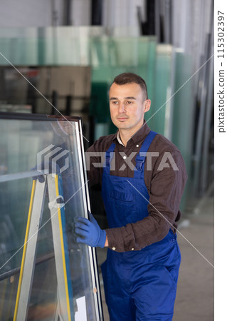 Portrait of man in blue overalls with window panes in glass workshop Portrait of man in blue overalls with window panes in glass workshop 115302397