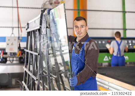 Portrait of man in blue overalls with window panes in glass workshop 115302422