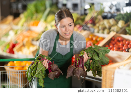 Saleswoman organizing fresh beets on display in organic food store Saleswoman organizing fresh beets on display in organic food store 115302501